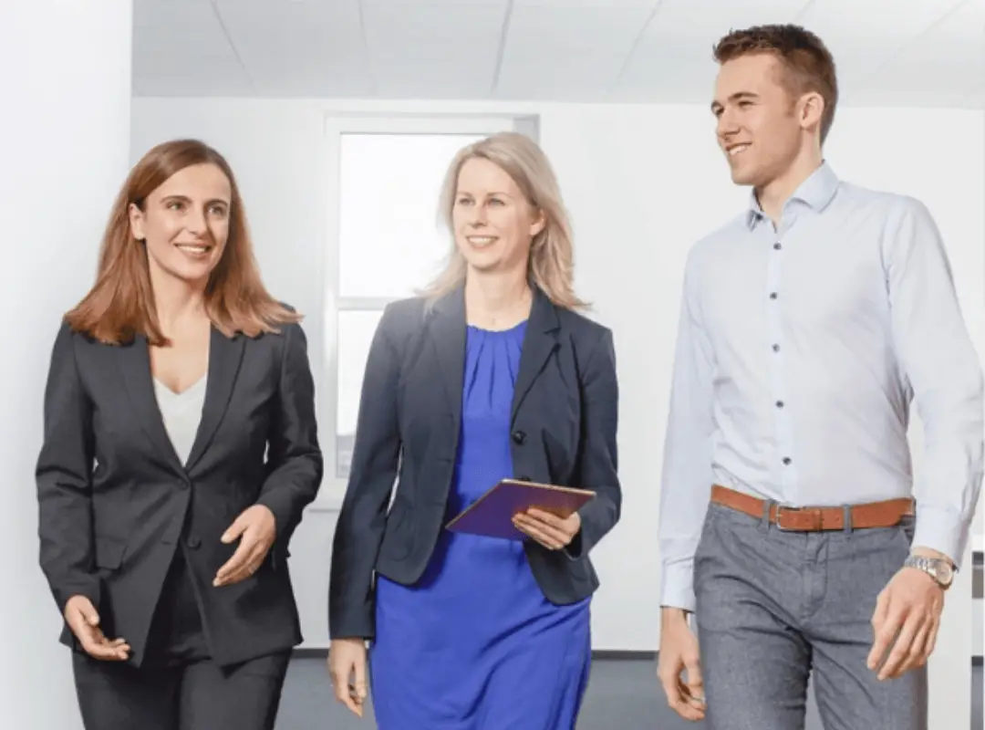 Zwei Mitarbeiterinnen und ein Mitarbeiter laufen gemeinsam durch einen Gang. 