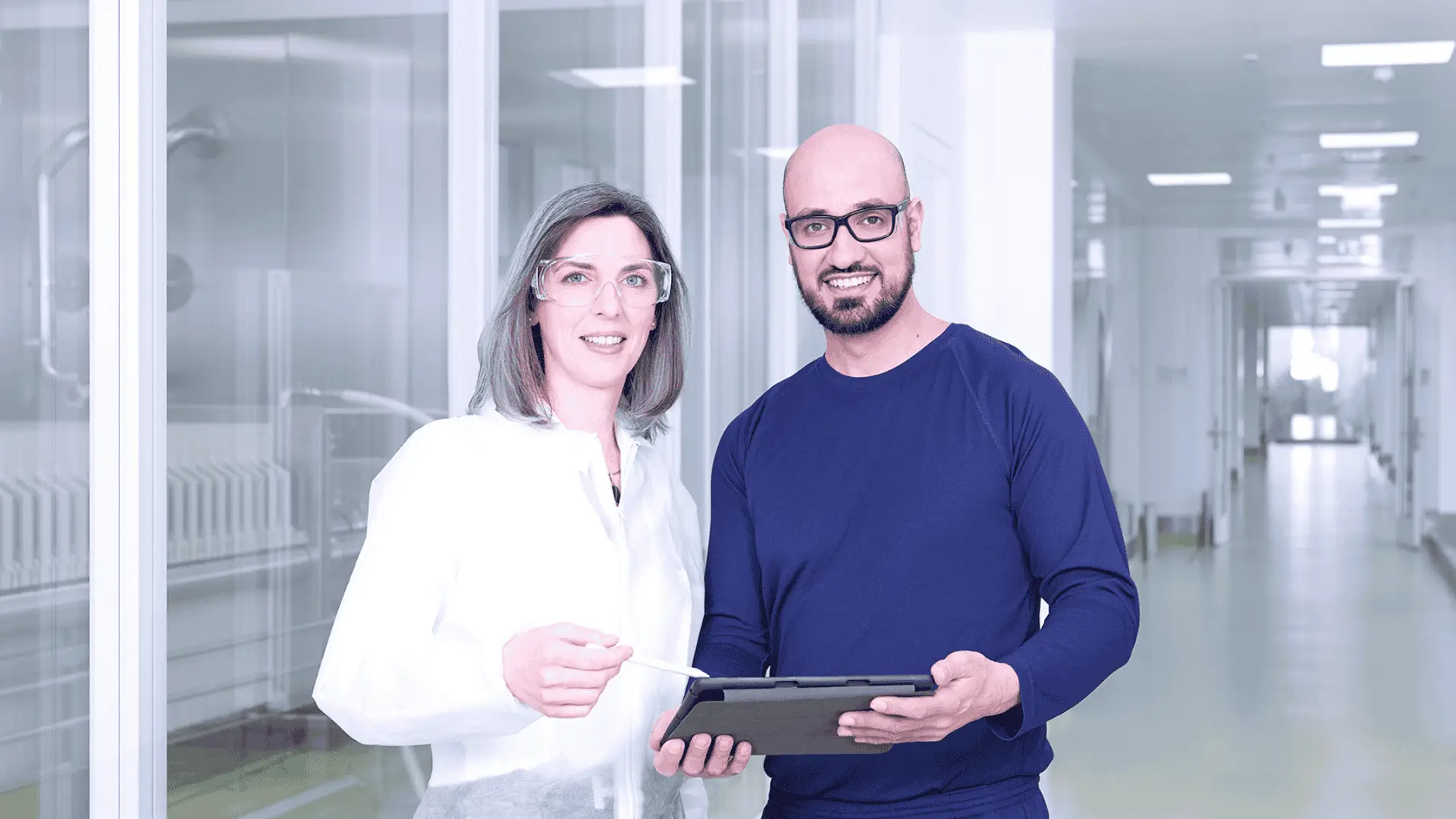 Zwei Kollegen stehen in einem Gang des neuen Produktionsgebäudes BNL und arbeiten zusammen an einem iPad.